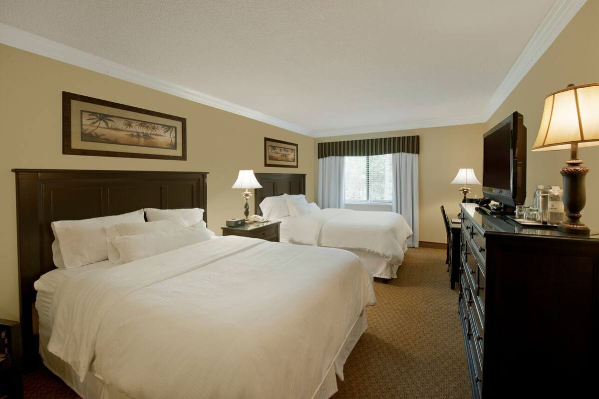 A hotel room with two beds, a desk, a dresser, and a television.