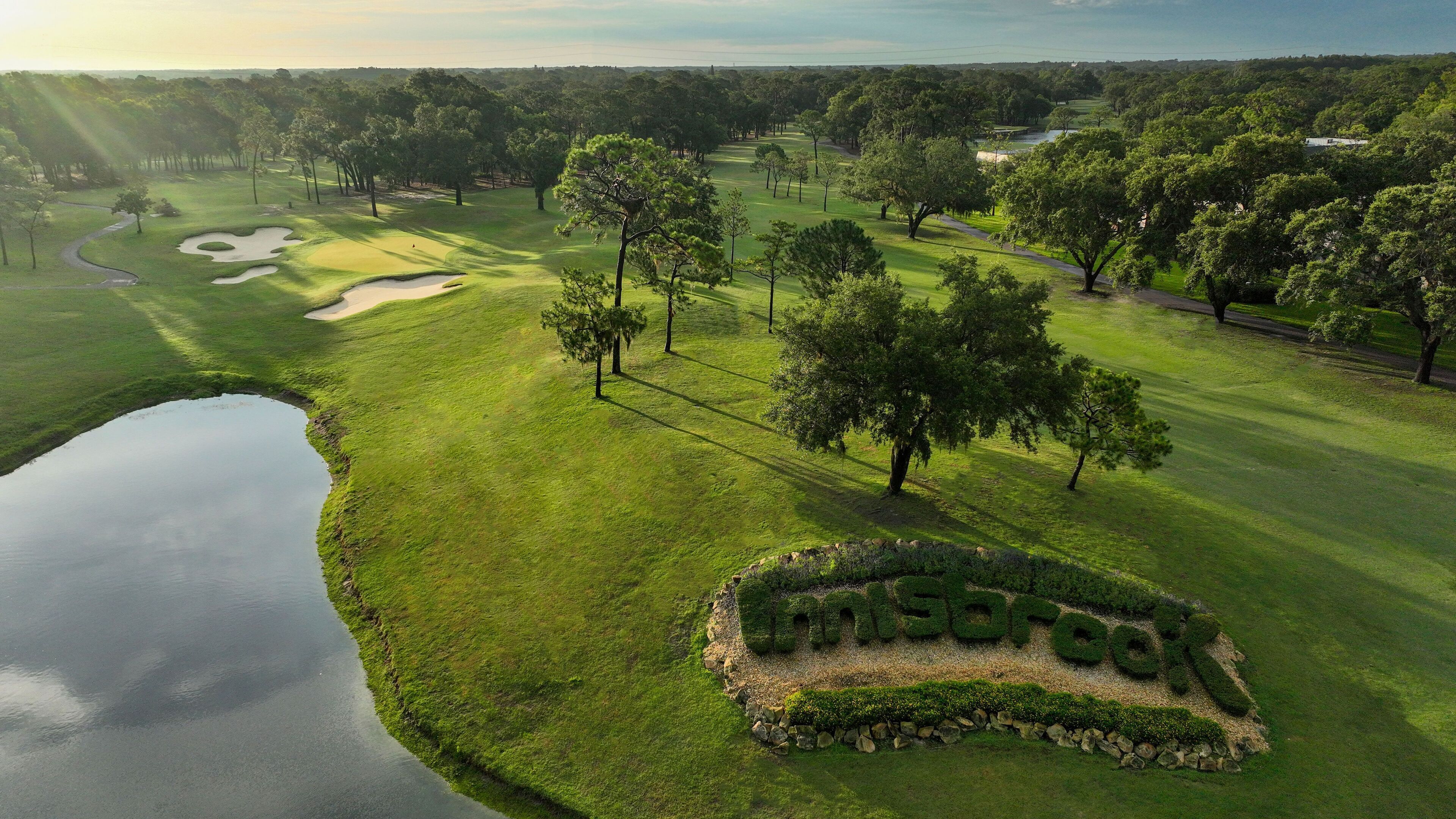 Un parcours de golf avec un étang, des arbres et un panneau indiquant « The Grove ».