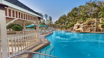 A swimming pool with a rock waterfall feature, surrounded by a wooden deck and lounge chairs.