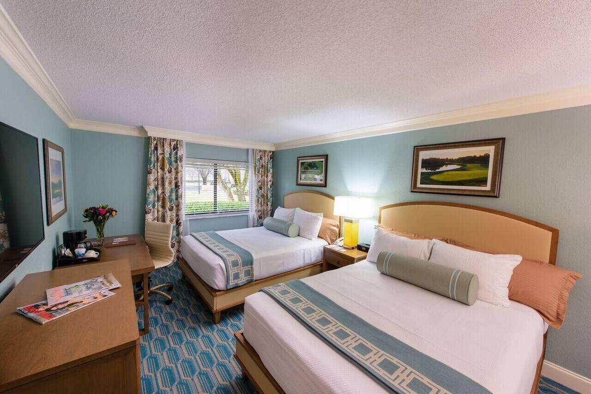 A hotel room with two beds, a desk, a chair, a lamp, and a window with curtains.