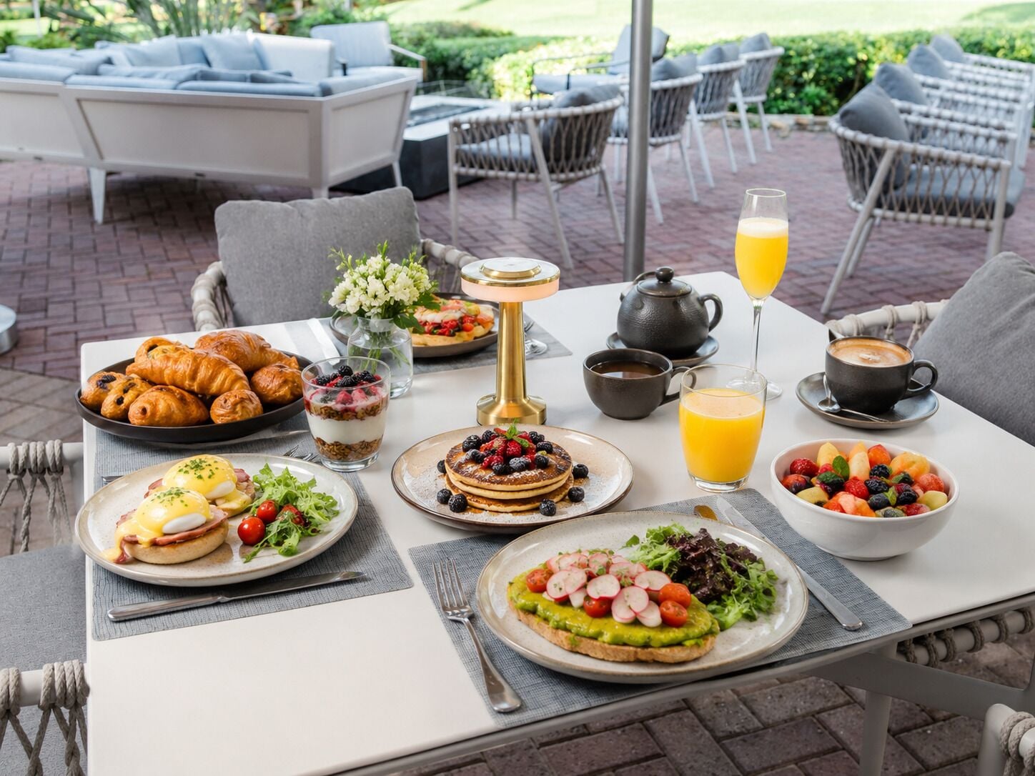 A breakfast setting with croissants, pancakes, eggs, and fresh fruit on a table.
