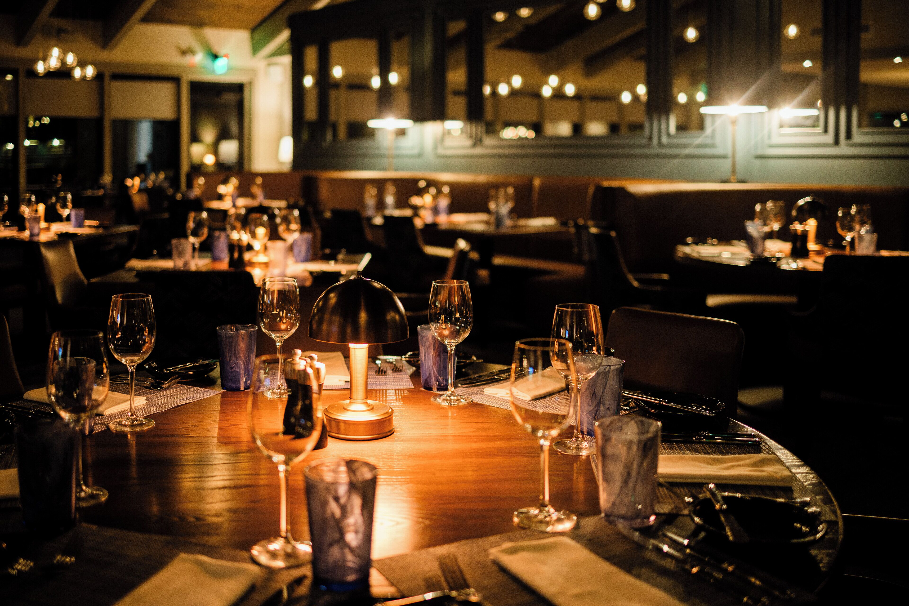 A restaurant interior with multiple dining tables, each set with wine glasses, plates, and cutlery.