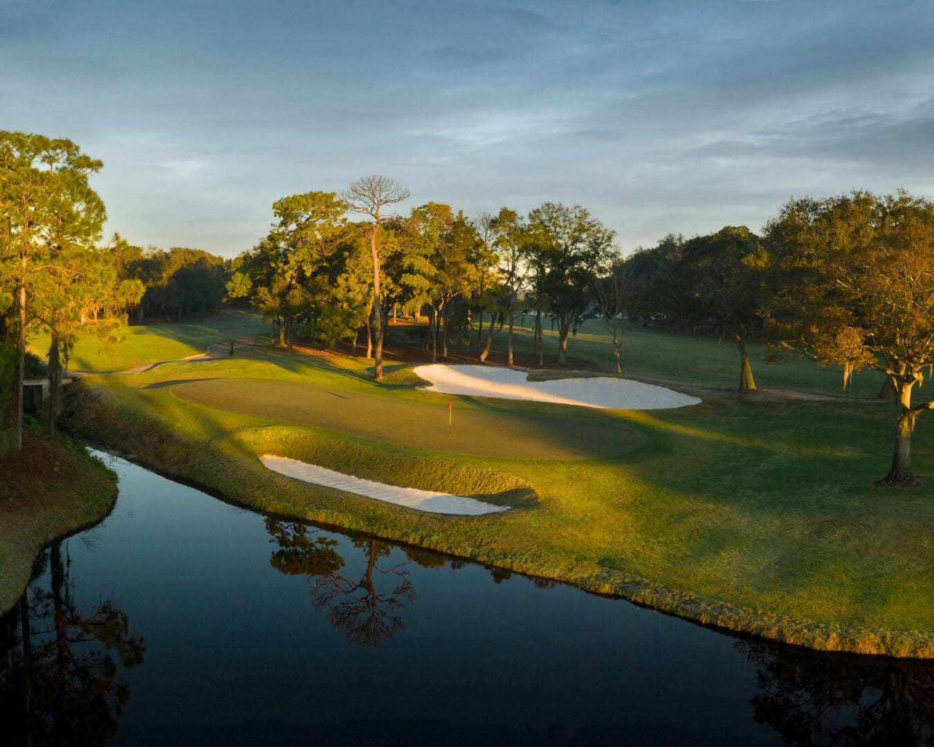A golf course with sand bunkers, a water body reflecting trees, and a clear sky.