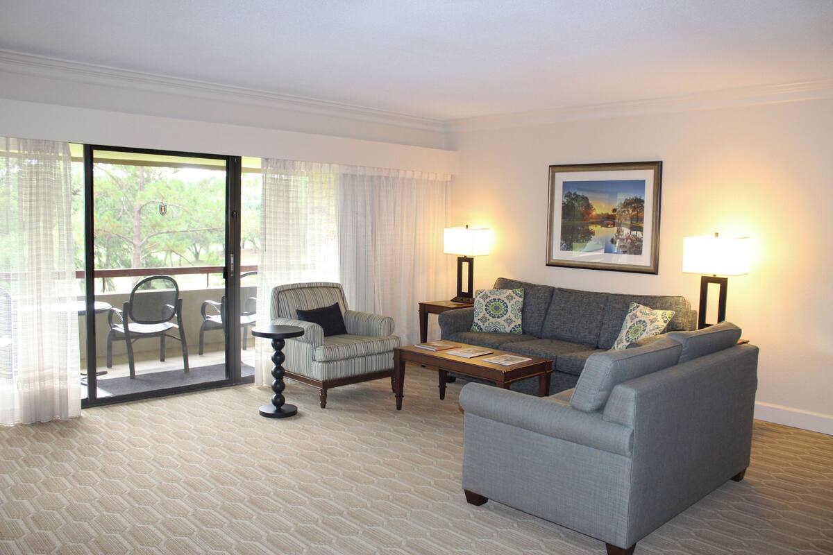 A hotel room with a grey sofa, armchairs, a coffee table, and a painting on the wall.