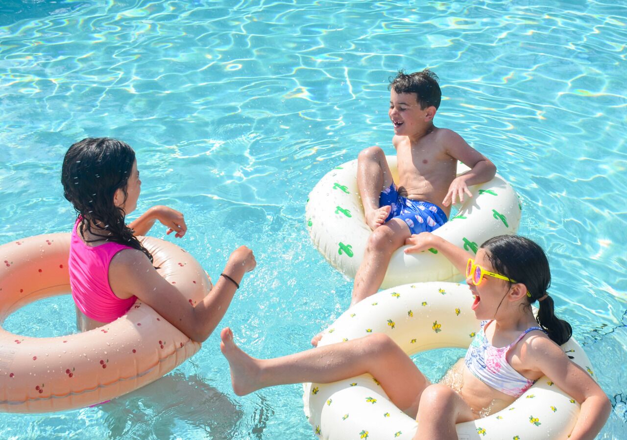 Three children in a swimming pool using inflatable rings.