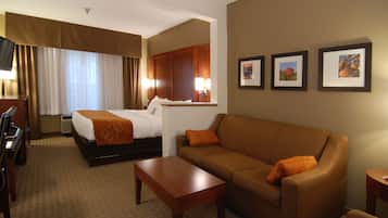 A hotel room with a bed, a sofa, a desk, and a chair. There are three framed pictures on the wall.