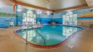 Una piscina interior con techo de madera, paredes de vidrio transparente y un mural de paisaje costero.
