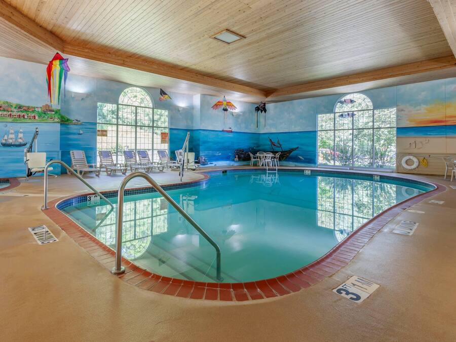 Una piscina interna con soffitto in legno, pareti di vetro trasparenti e un affresco raffigurante una scena costiera.