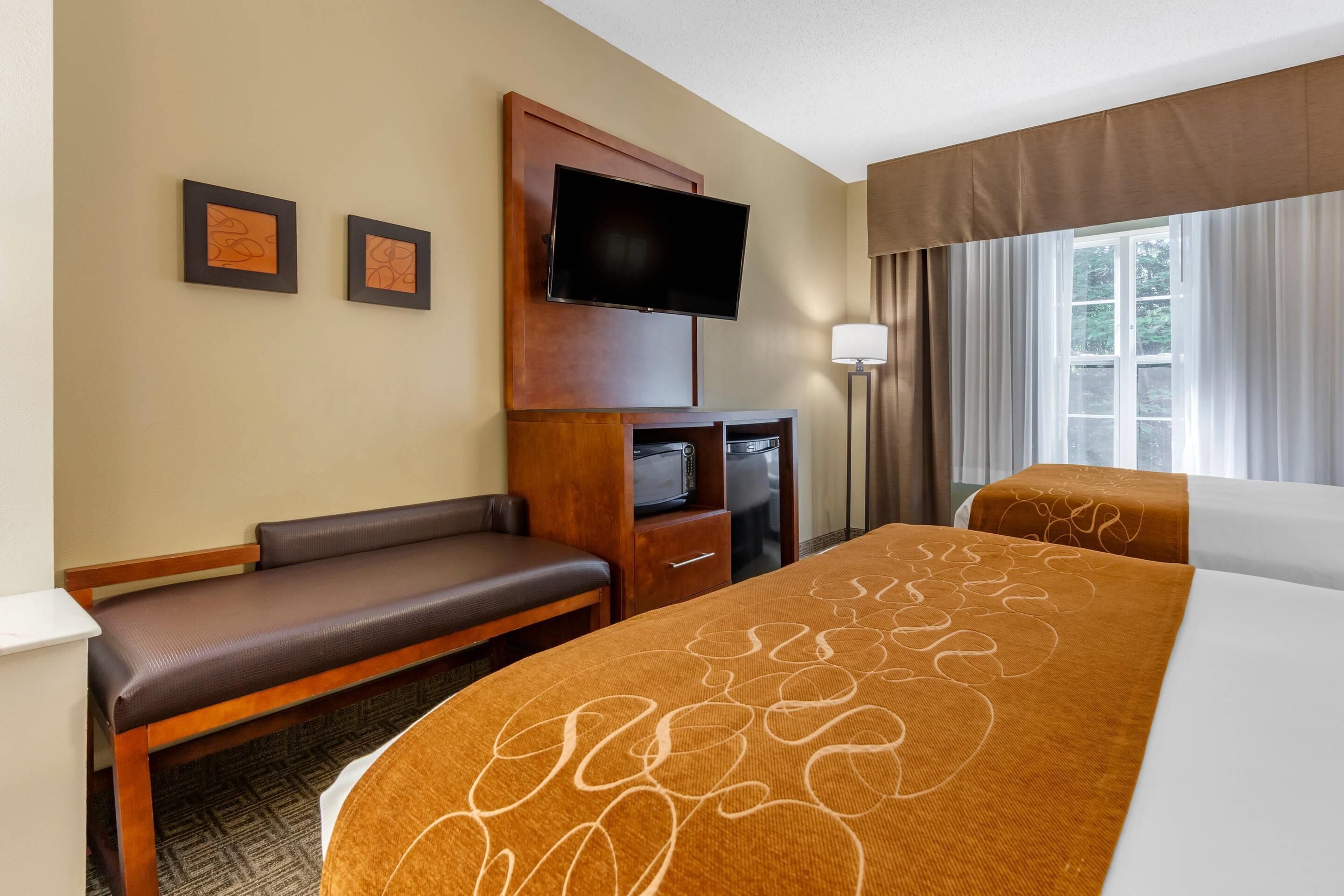 Habitación de hotel con cama, escritorio, televisor y dos cuadros en la pared.