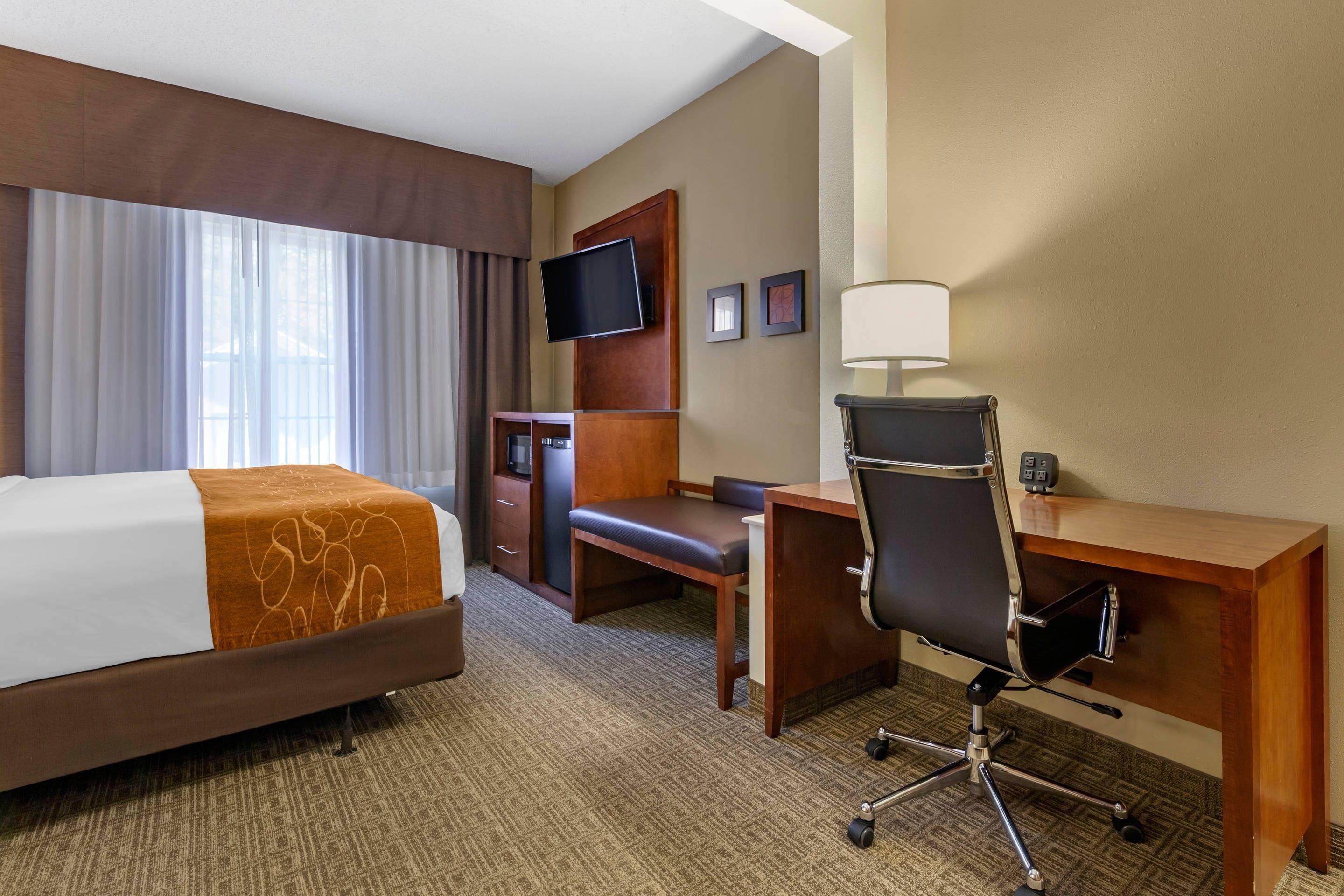 A hotel room with a bed, desk, chair, television, and lamp.