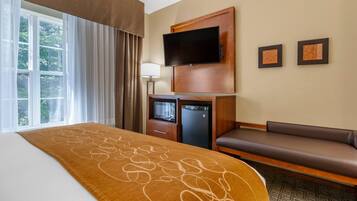A hotel room with a bed, a TV mounted on the wall, a small refrigerator, a sofa, and two framed pictures on the wall.