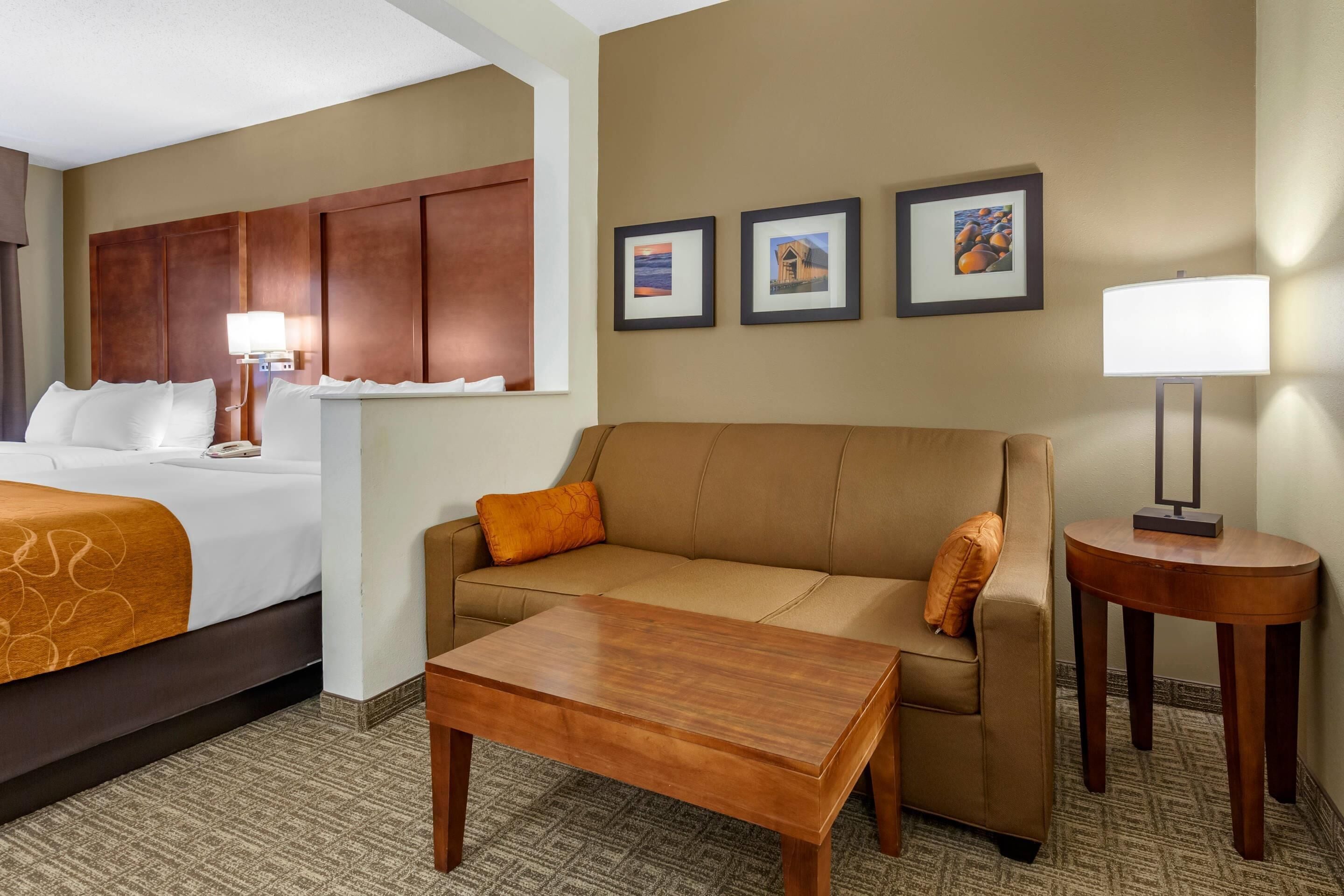 Una habitación de hotel con una cama, un sofá, una mesita de centro y una pequeña mesa con lámpara.