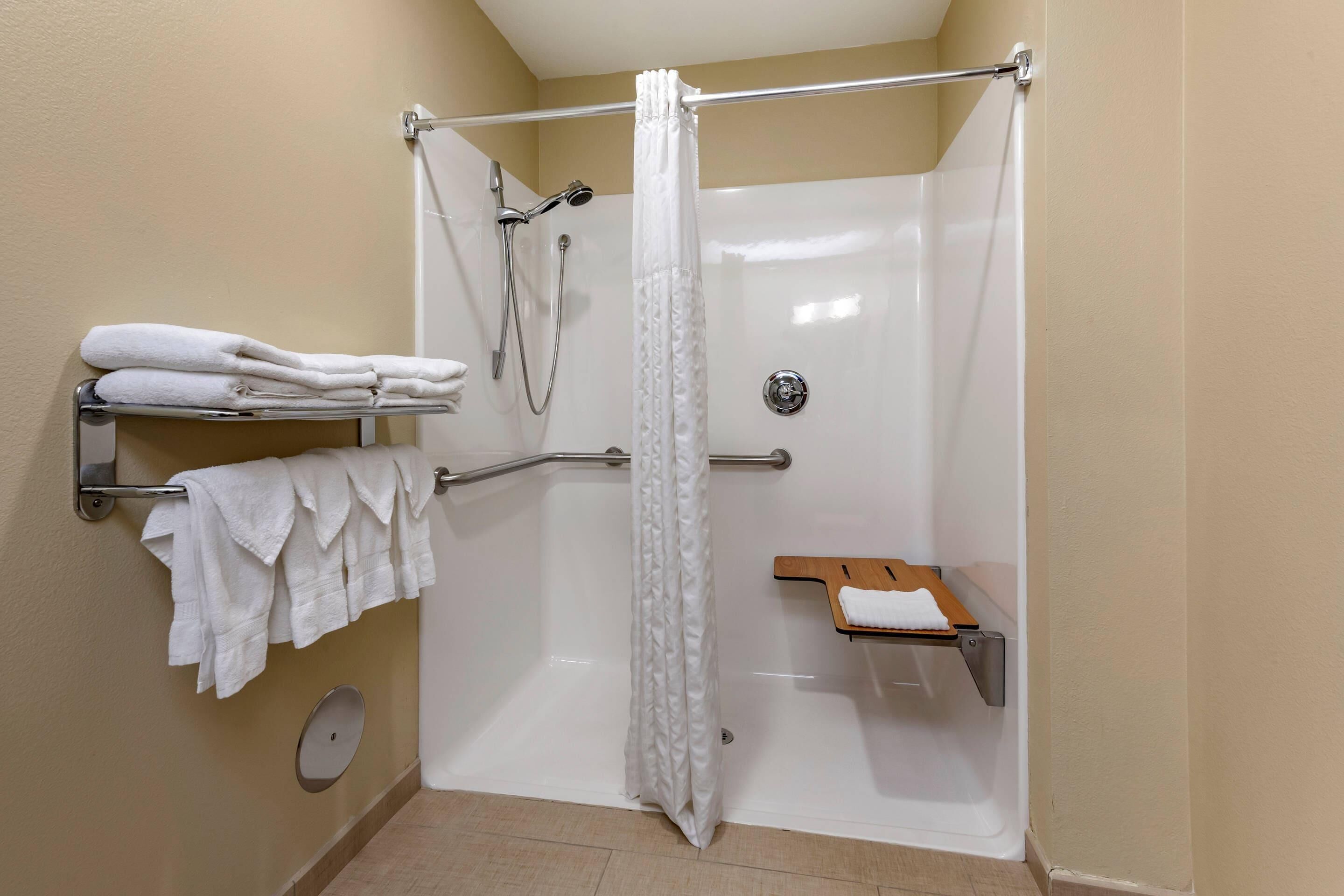 A shower area with a white shower curtain, a handheld showerhead, a grab bar, and a shelf with towels.