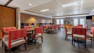 A spacious dining area with multiple tables and chairs, wooden paneling on the walls, and a ceiling with recessed lighting.