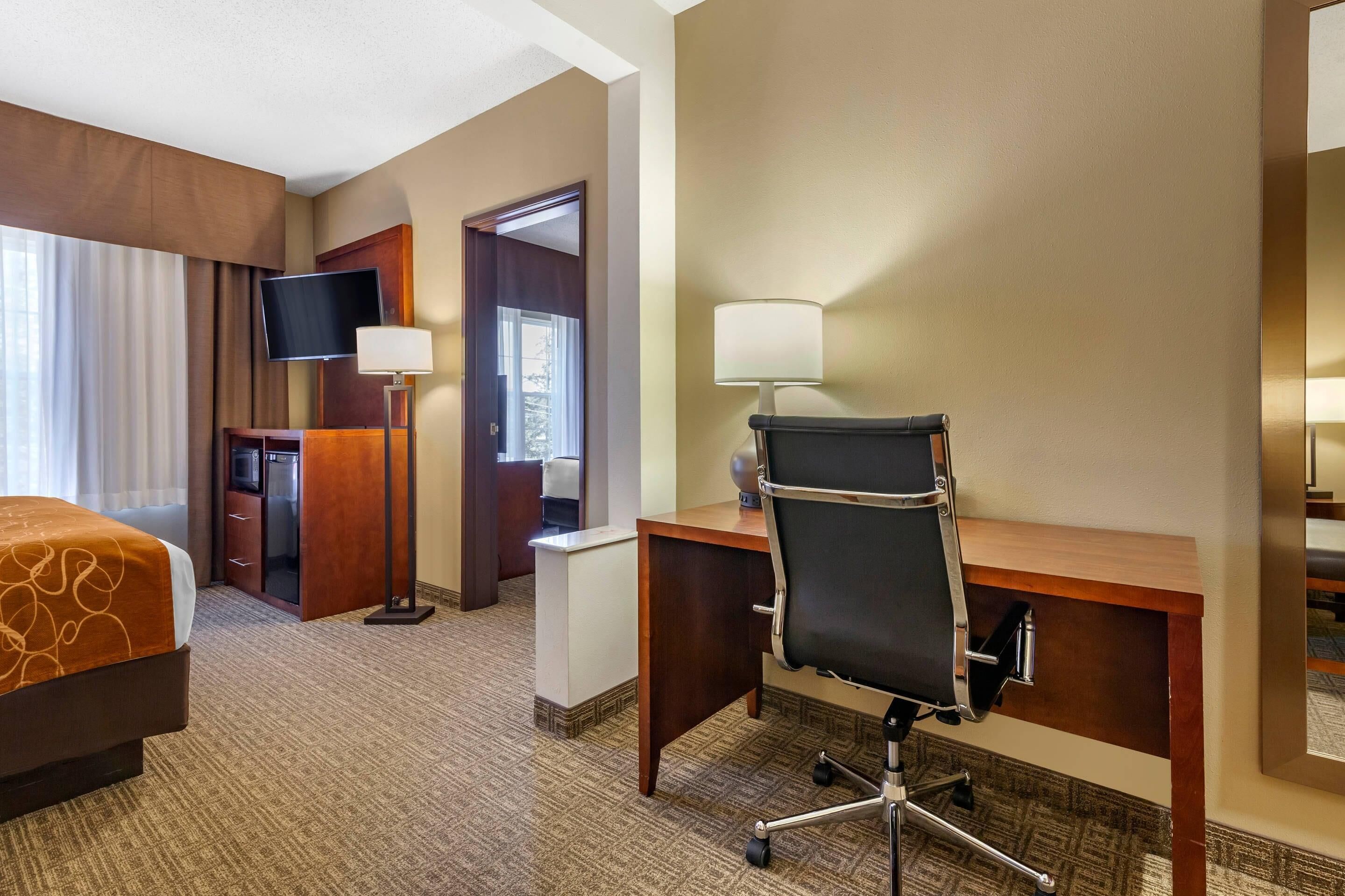 A hotel room with a bed, desk, chair, TV, and a door leading to a bathroom.