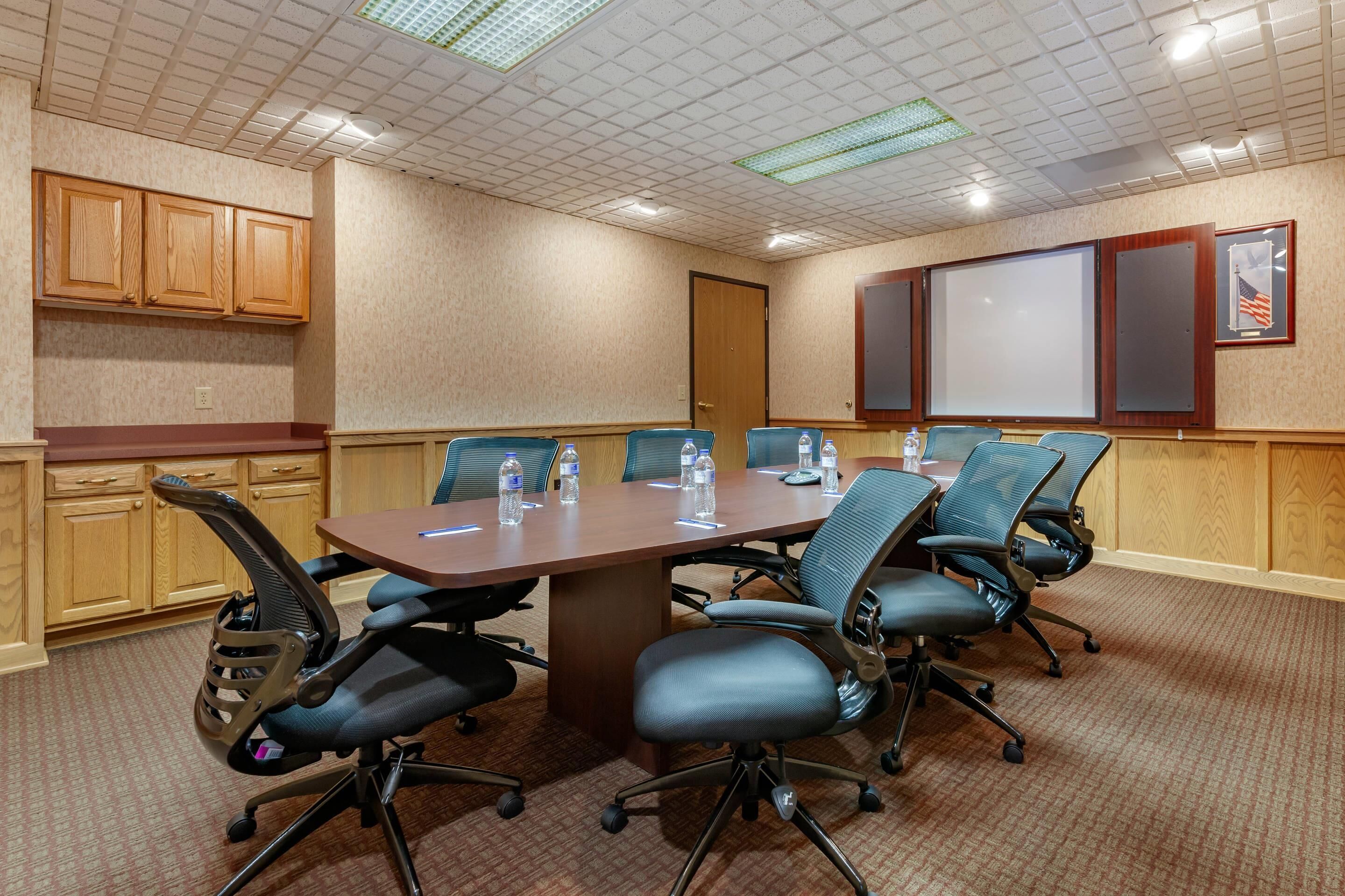 Una sala de conferencias con una mesa larga, seis sillas y una pantalla de proyector.