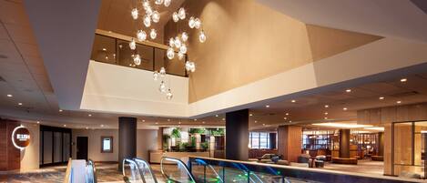 A modern hotel lobby with escalators, a reception area, and a bar.