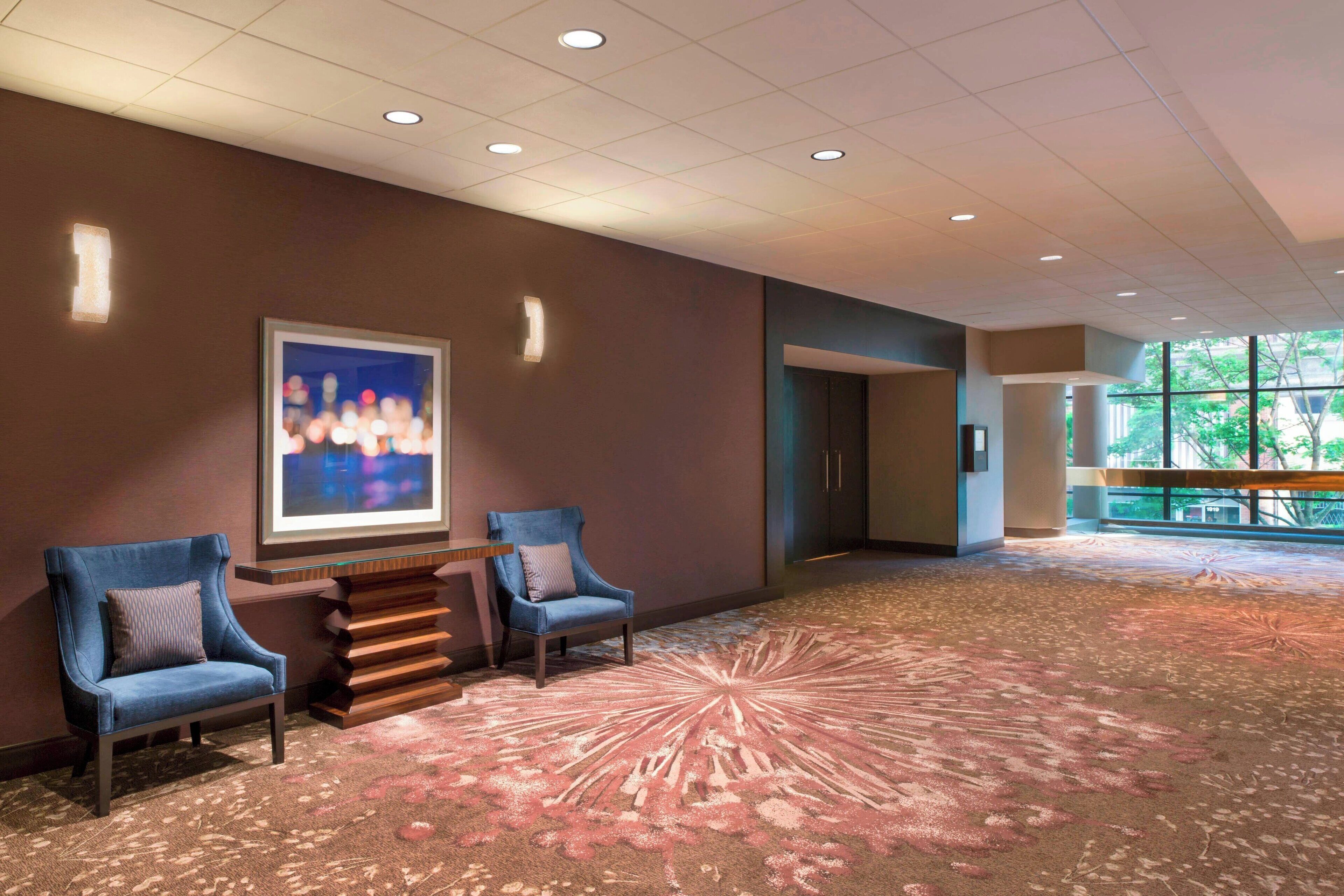 A hotel lobby with two armchairs, a large abstract painting, and a patterned carpet.