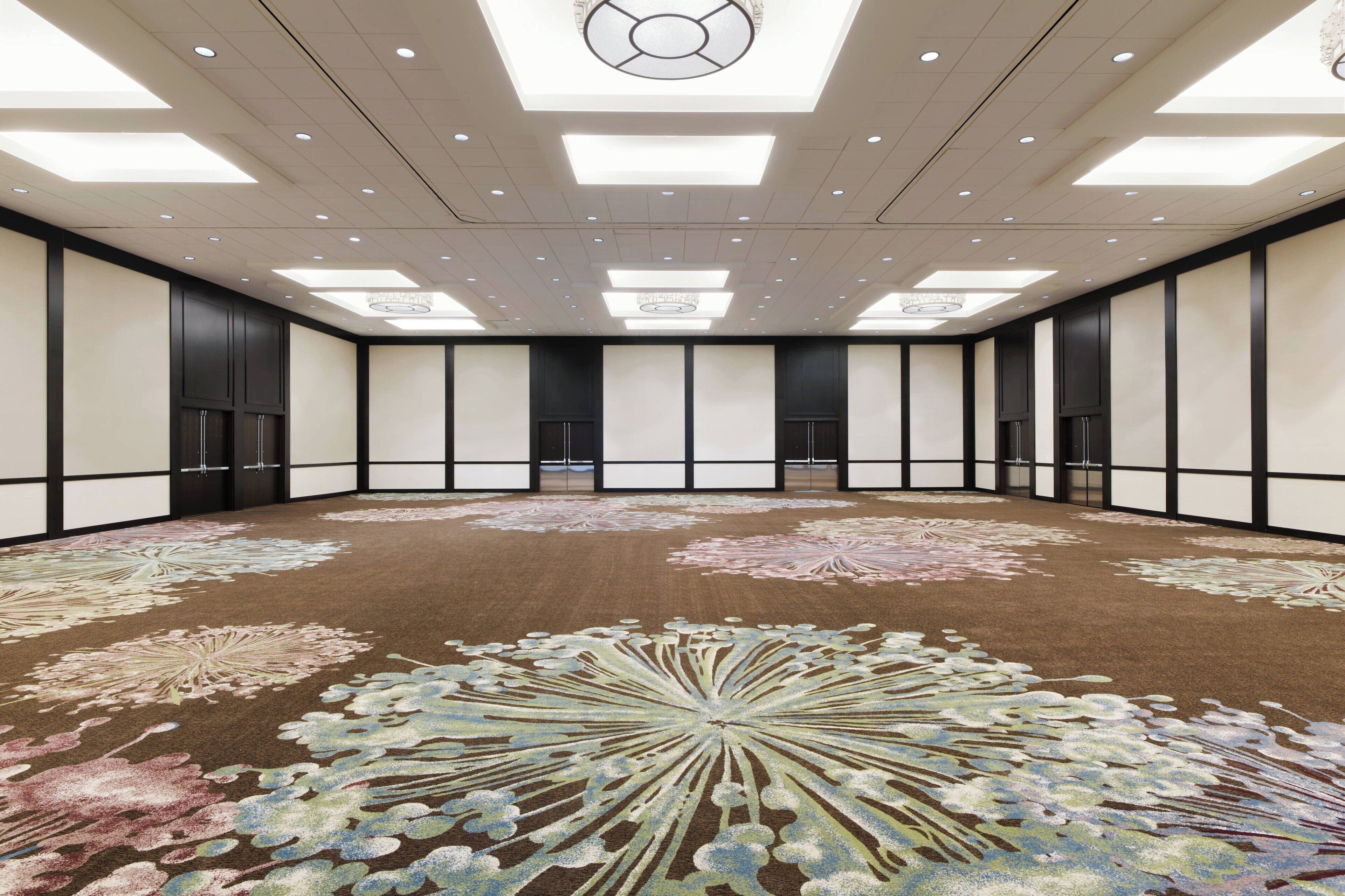 Une grande salle de conférence, bien éclairée, dotée d’un tapis à motifs et d’un plafond haut avec des luminaires encastrés.