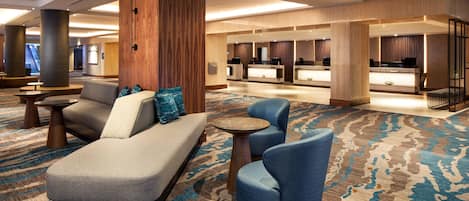 Un vestíbulo de hotel con una recepción, zona de estar con sofás y sillones, y una alfombra estampada.