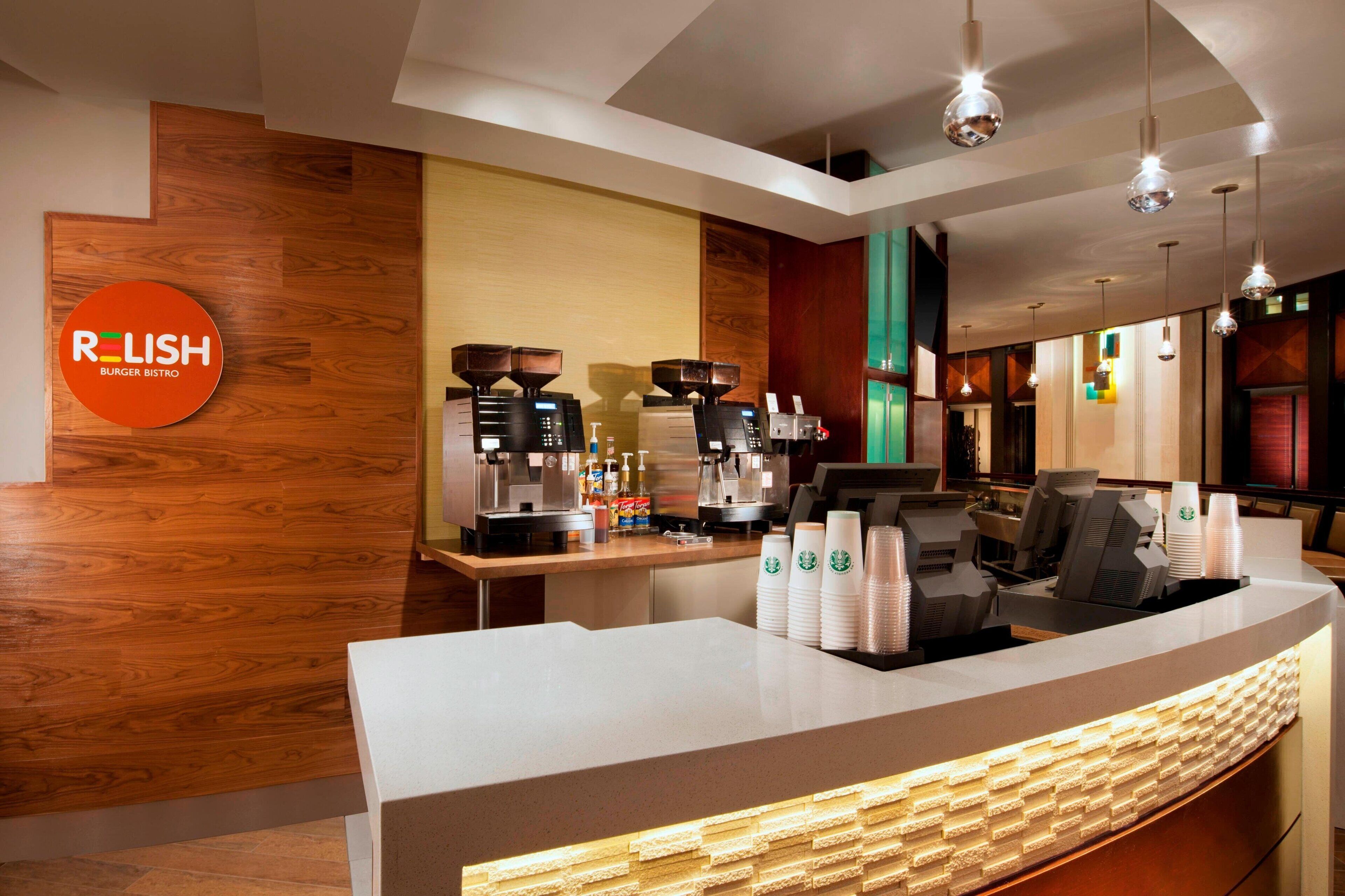 A modern restaurant interior with a wooden accent wall, a counter with stacked cups, and a coffee machine.