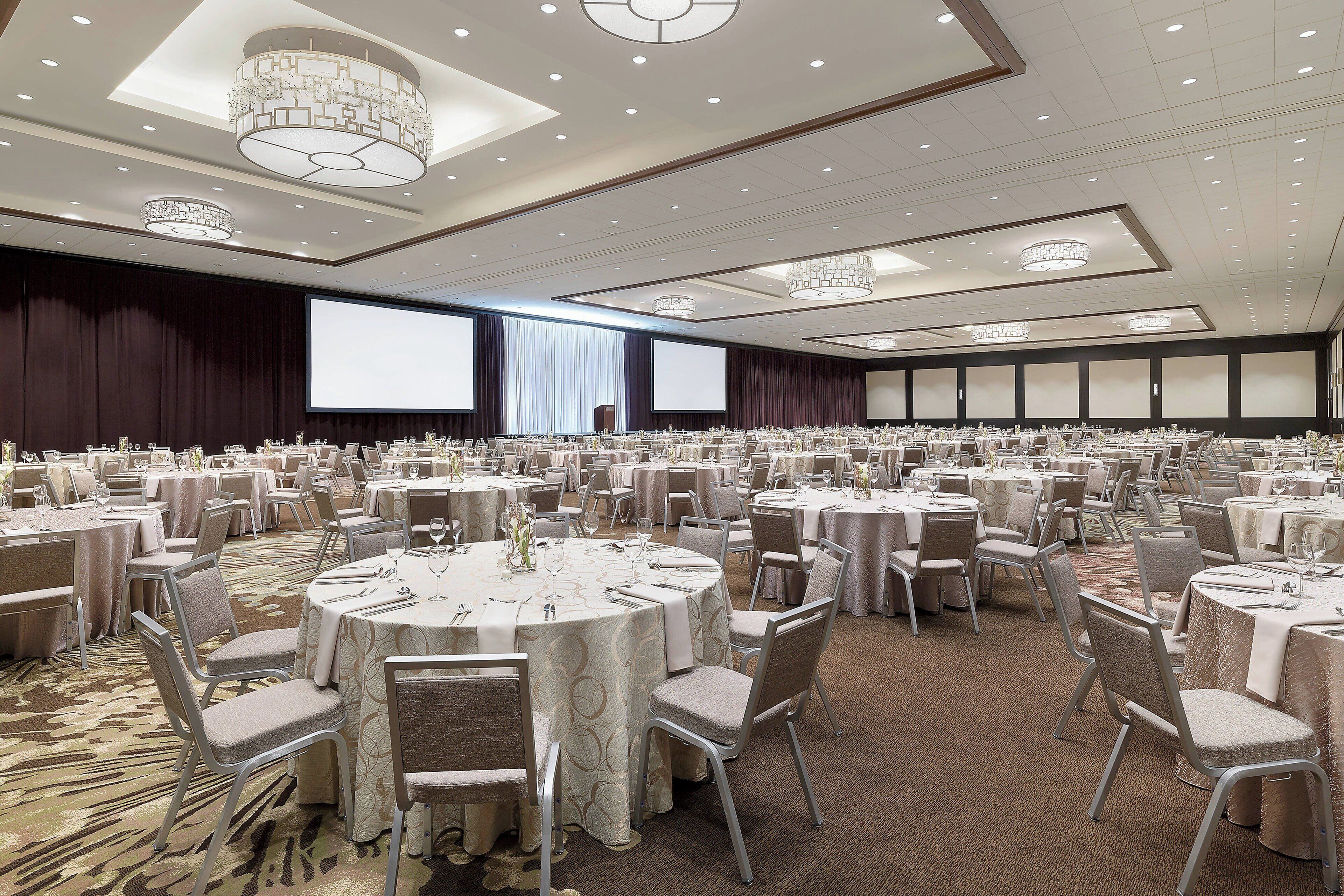 Une grande salle de banquet avec des tables rondes, des chaises et un grand écran à l’avant.
