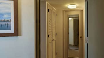 Un pasillo de hotel con un cuadro enmarcado de una vista urbana en la pared, una puerta con espejo y una lámpara en el techo.