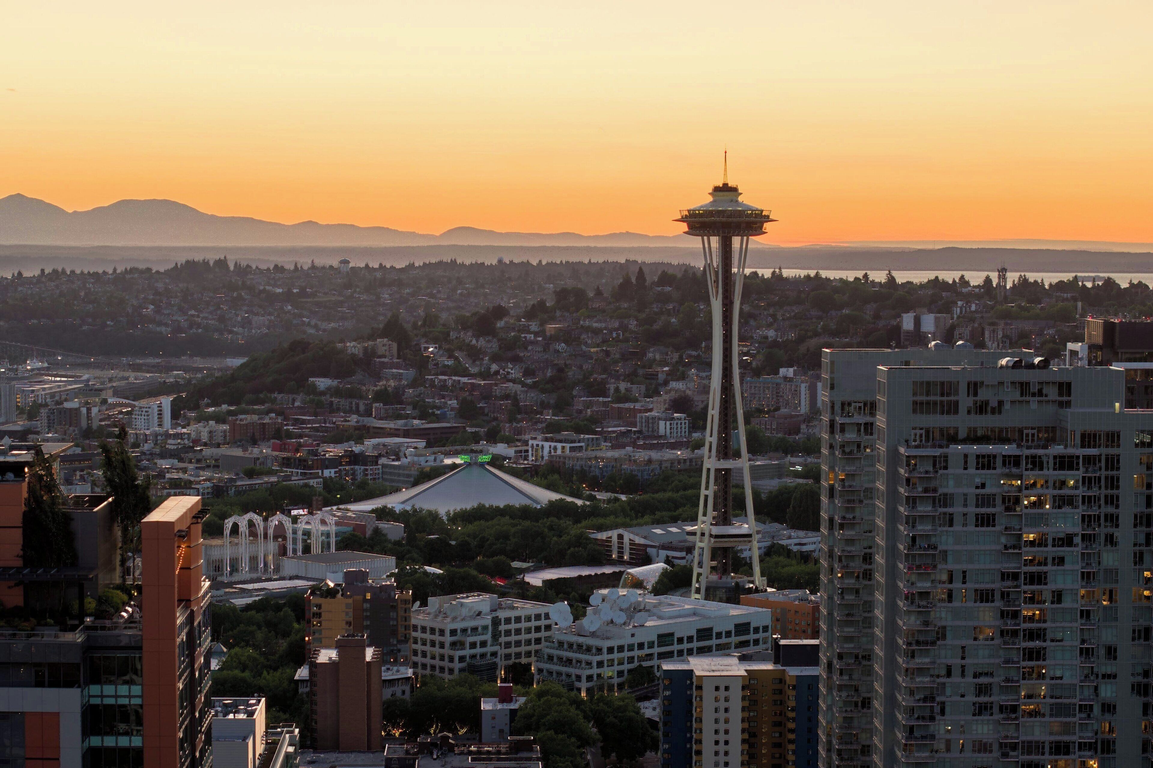 A cityscape with a prominent tower, dense urban buildings, and a distant mountain range.