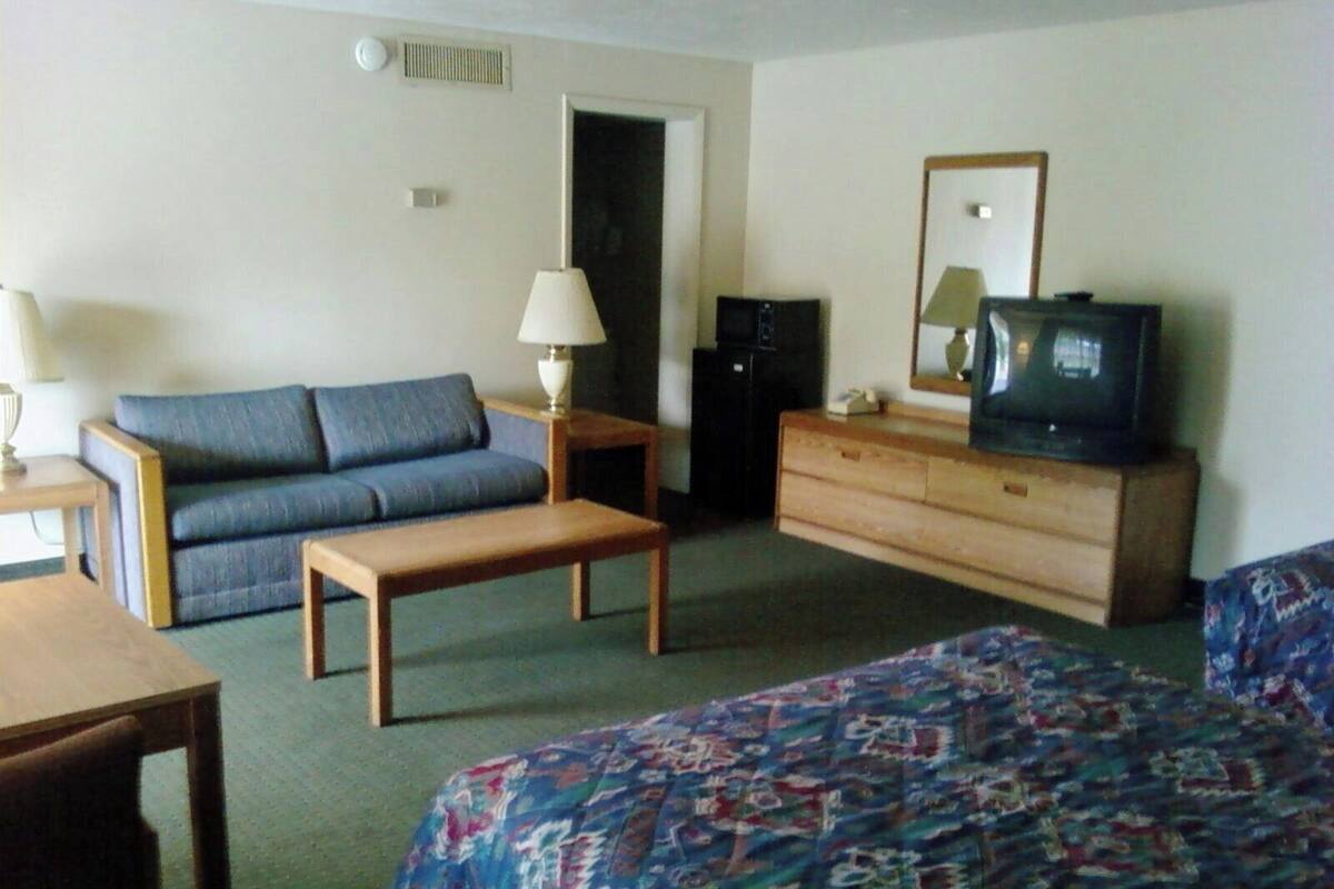 A hotel room with a bed, a sofa, a small table, a dresser, a television, and a microwave.