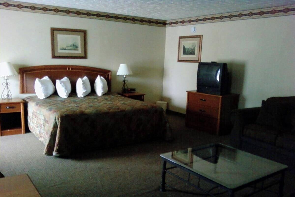 A hotel room with a bed, a television, a glass coffee table, a sofa, and two bedside tables with lamps.