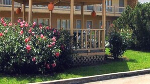 A hotel with a covered outdoor area, a pool, and a well-maintained garden. - Will Rogers Inn (Claremore)