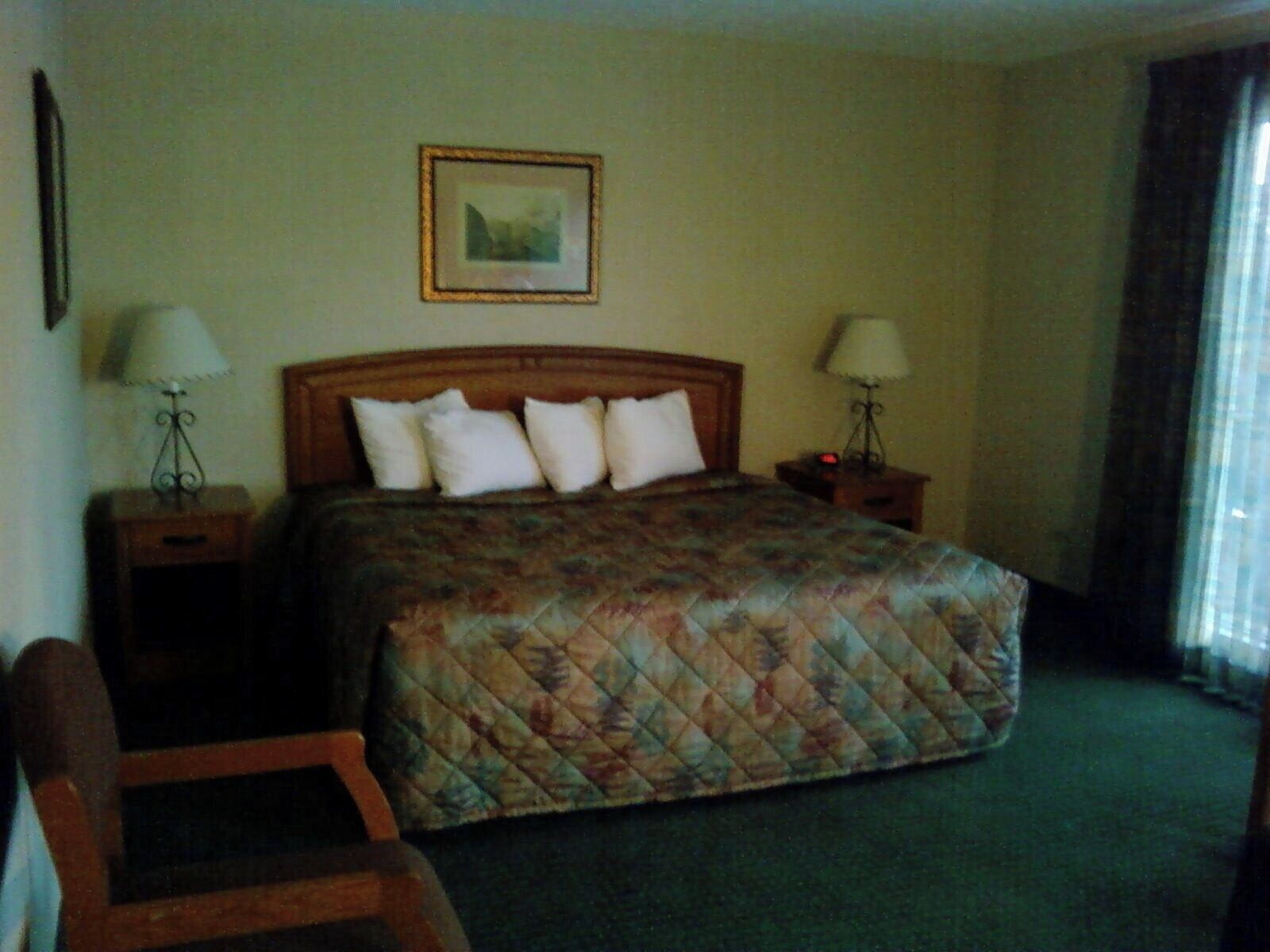 A hotel room with a bed, two bedside tables, a chair, a framed picture on the wall, and a window with curtains.