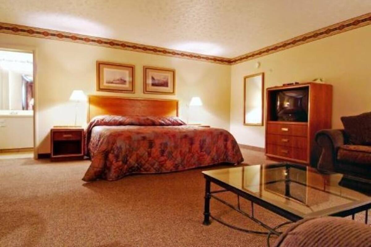 A hotel room with a bed, a glass coffee table, a wooden cabinet, a sofa, and two framed pictures on the wall.
