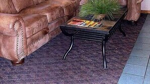 A living room with a brown leather sofa, a matching armchair, a small table with a plant, and framed pictures on the wall. - Will Rogers Inn (Claremore)