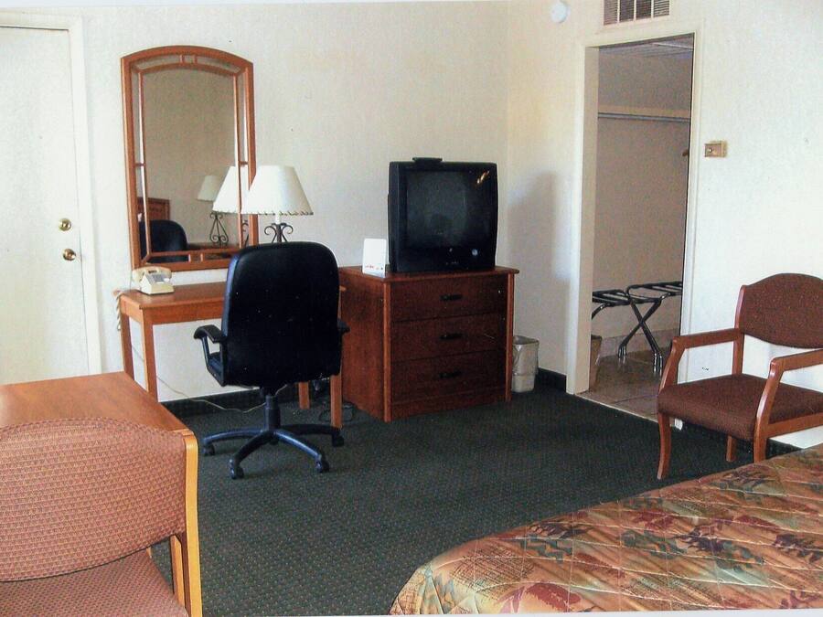 Et hotelværelse med seng, skrivebord med computer, stol, fjernsyn, spejl og garderobeskab.