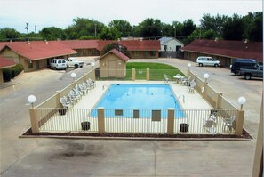 Una piscina con un borde cercado, rodeada de edificios de motel con techos rojos.