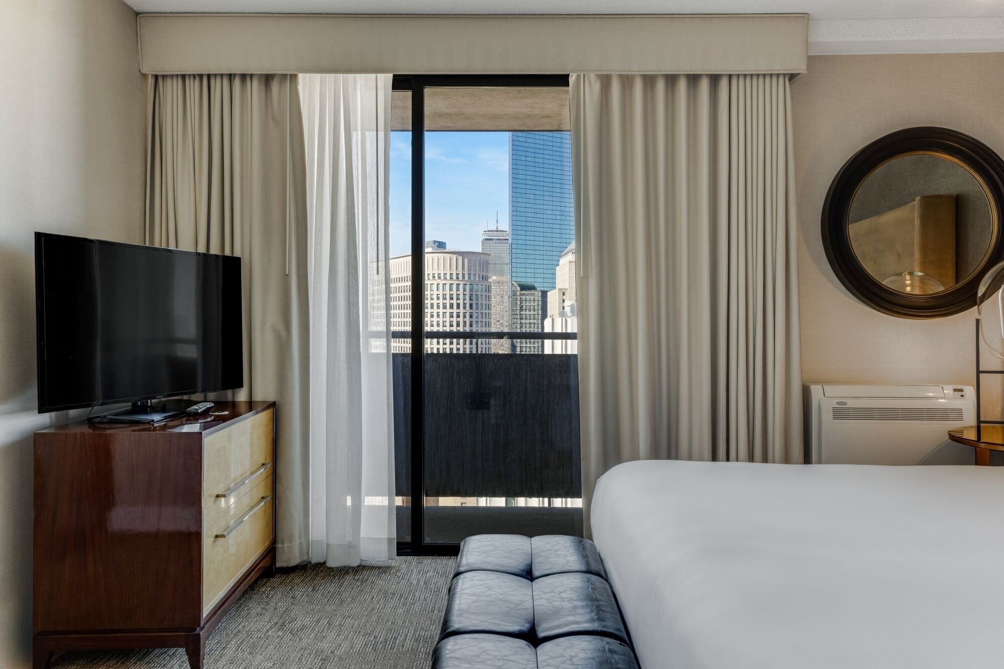 Una habitación de hotel con cama, televisión, cómoda, espejo y vistas a la ciudad.