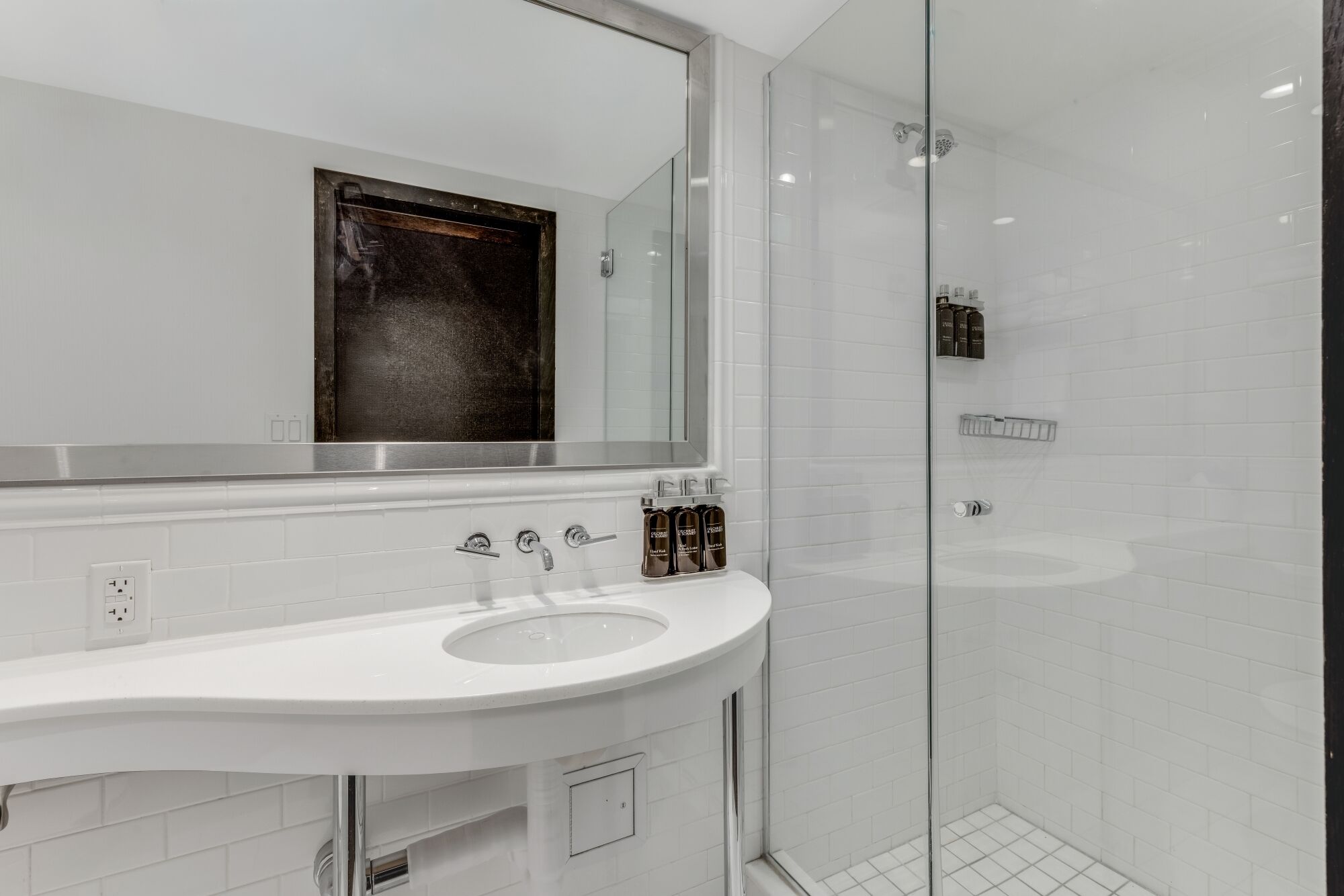 A modern bathroom with a large mirror, a white sink, and a glass-enclosed shower.