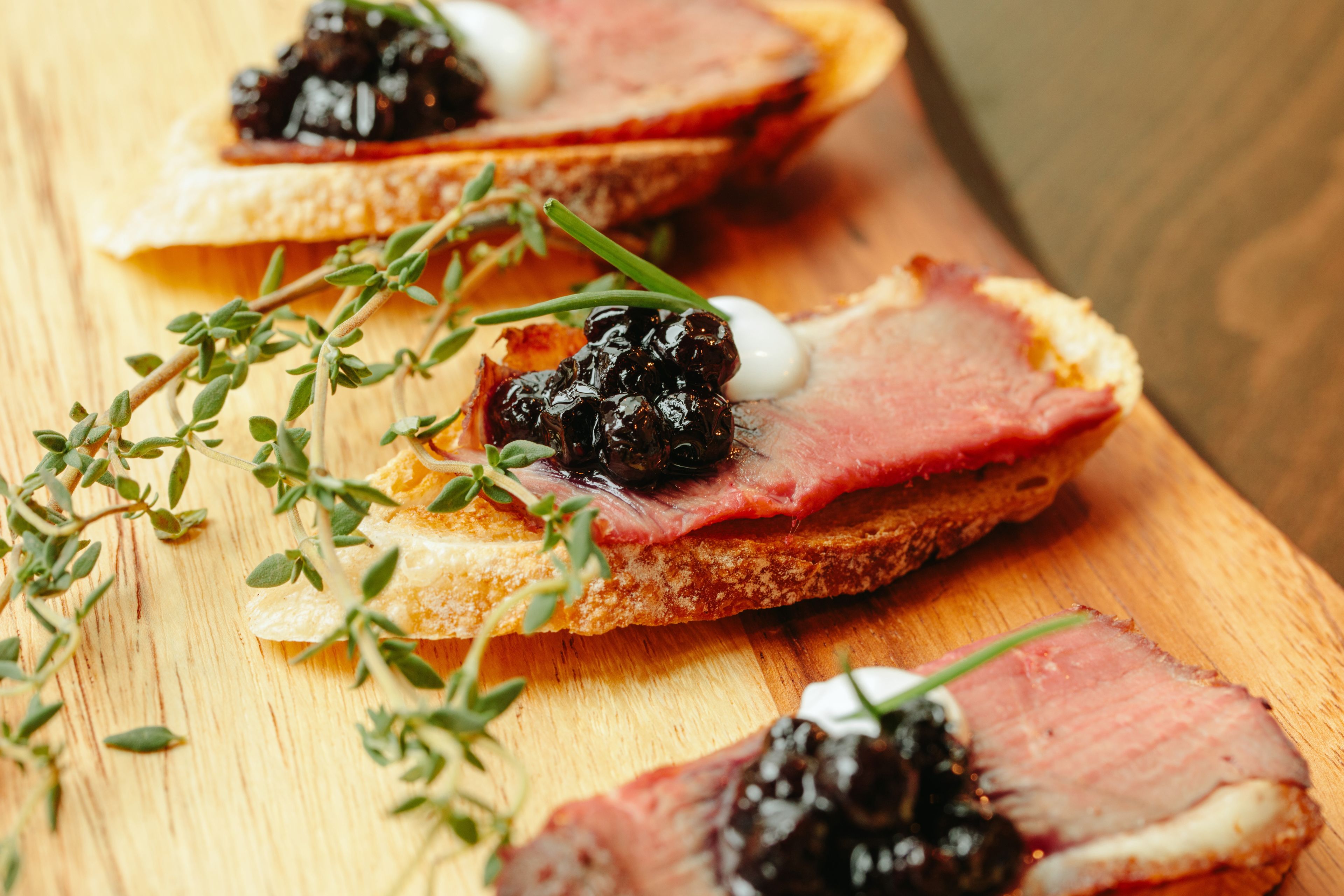 A wooden cutting board with slices of meat and caviar on toast, garnished with herbs.