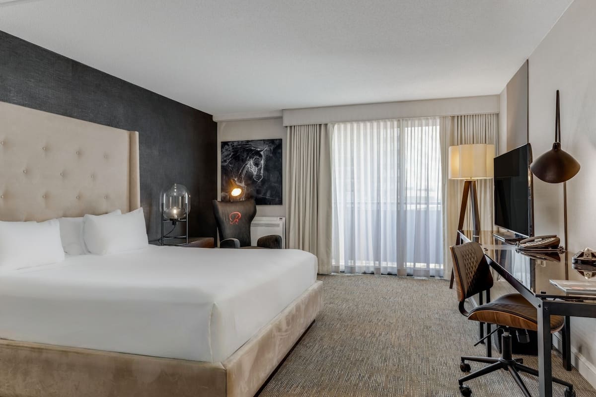 Ein Hotelzimmer mit einem großen Bett, einem Schreibtisch mit Stuhl, einem Fernseher und einer Lampe.