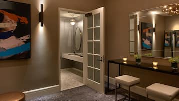 A modern bathroom with a glass door, a large mirror, a sink, and a bench.