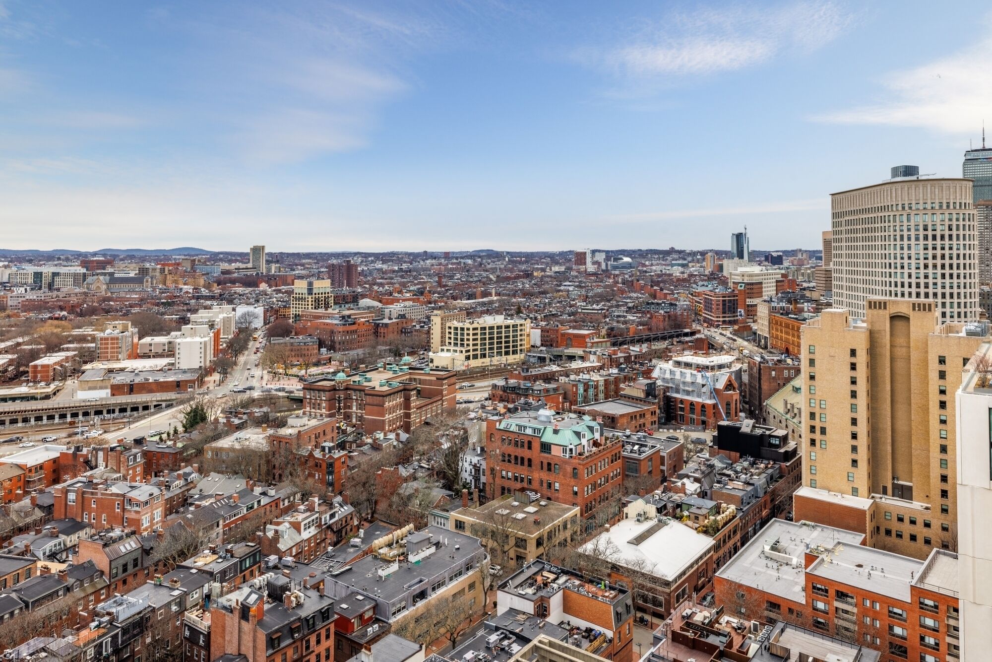 A cityscape with a mix of historic and modern buildings, a prominent red-brick structure, and a large, cylindrical building on the right.
