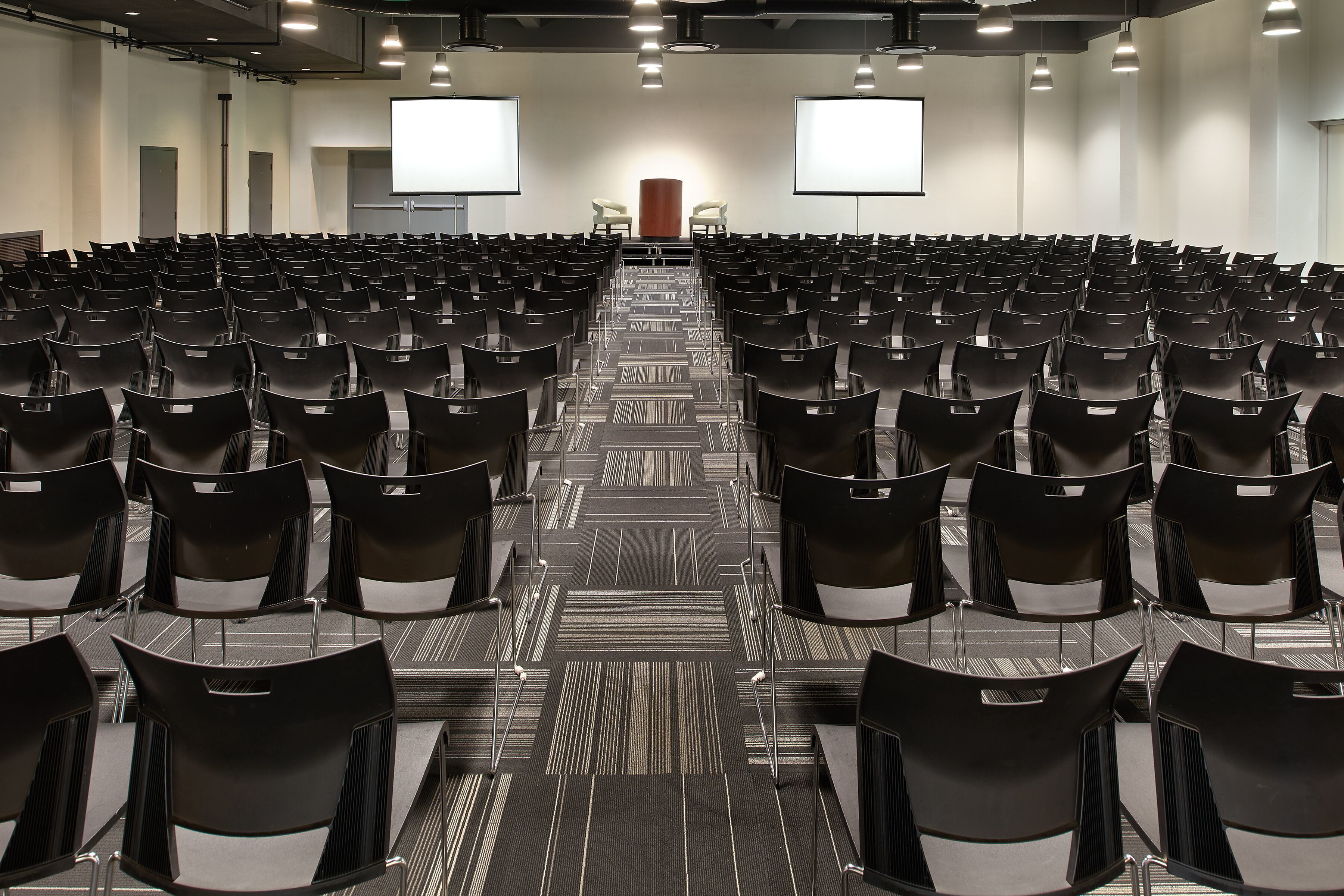A conference room with rows of chairs, a podium, and two projection screens.