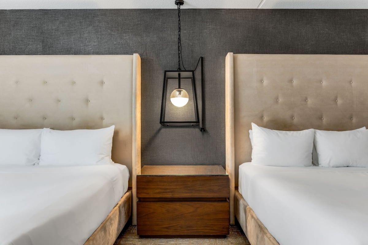 Ein Hotelzimmer mit zwei Betten, einem hölzernen Nachttisch, einer Pendelleuchte und einer strukturierten Wand.