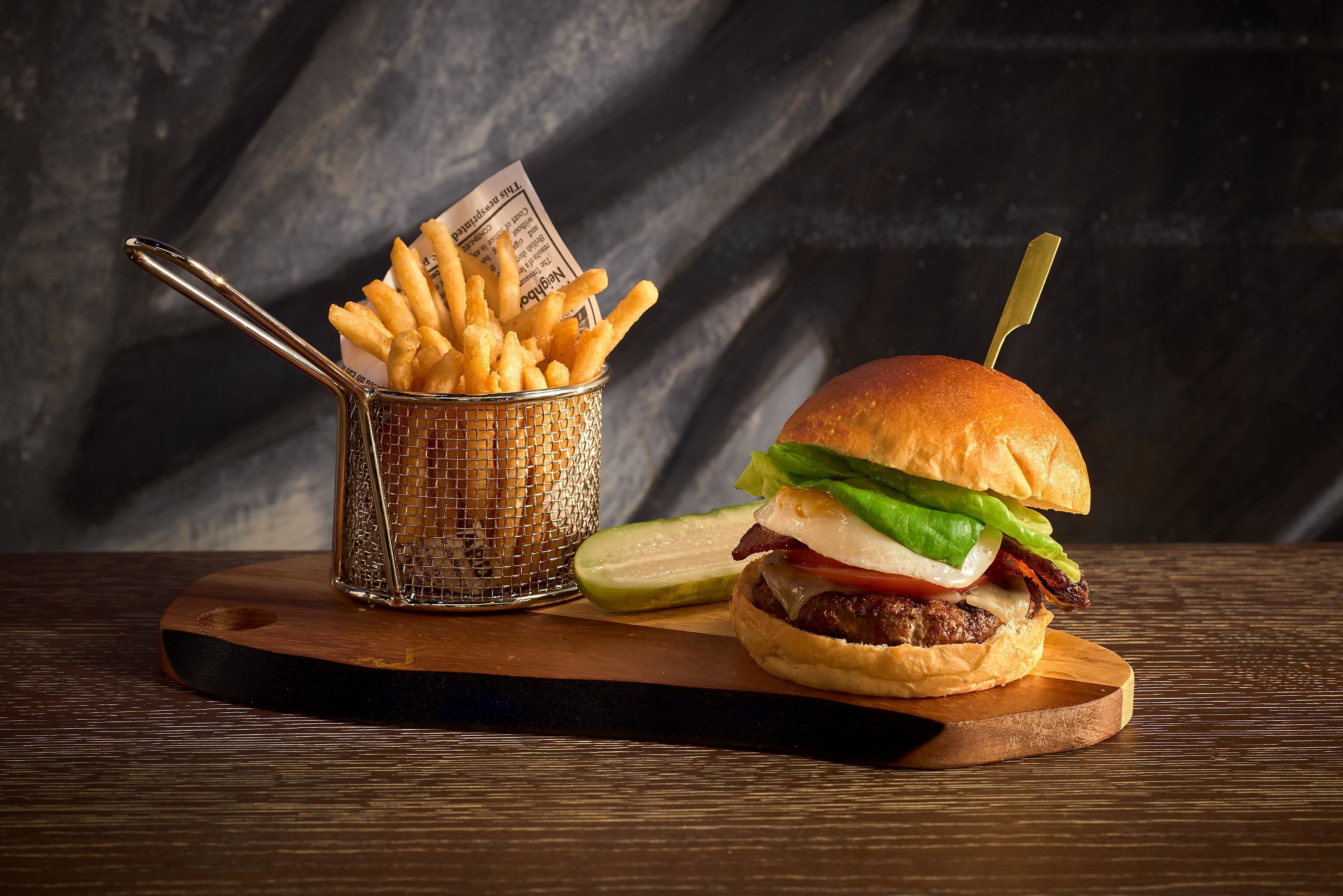 A burger with fries and a pickle on a wooden board.