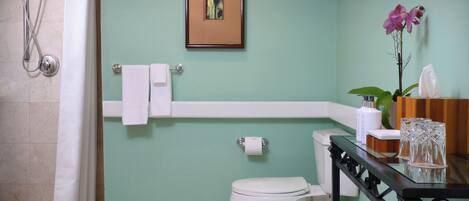 A bathroom with a shower, toilet, and a sink area with a towel rack and a framed picture on the wall.