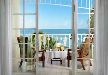 A hotel room with a bed, a sofa, a desk with a computer, a chair, and a view of the sea through large windows. at Ocean Key Resort - A Noble House Resort