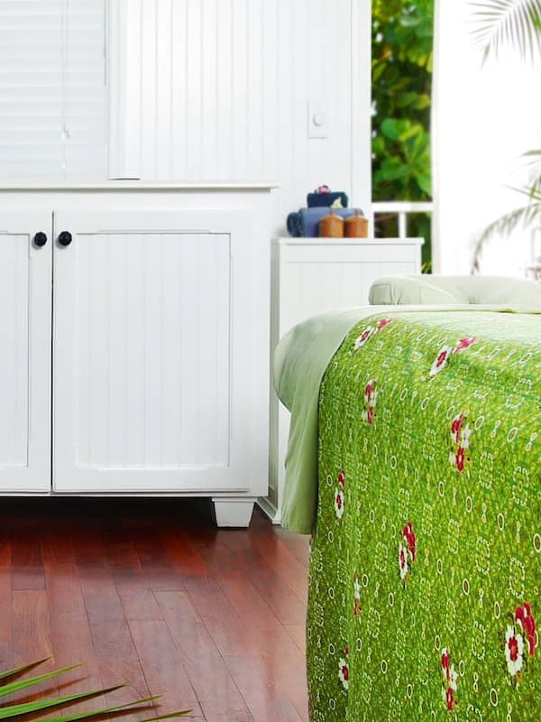 Two single beds with floral-patterned bedspreads, a cabinet, and a small table with a potted plant.