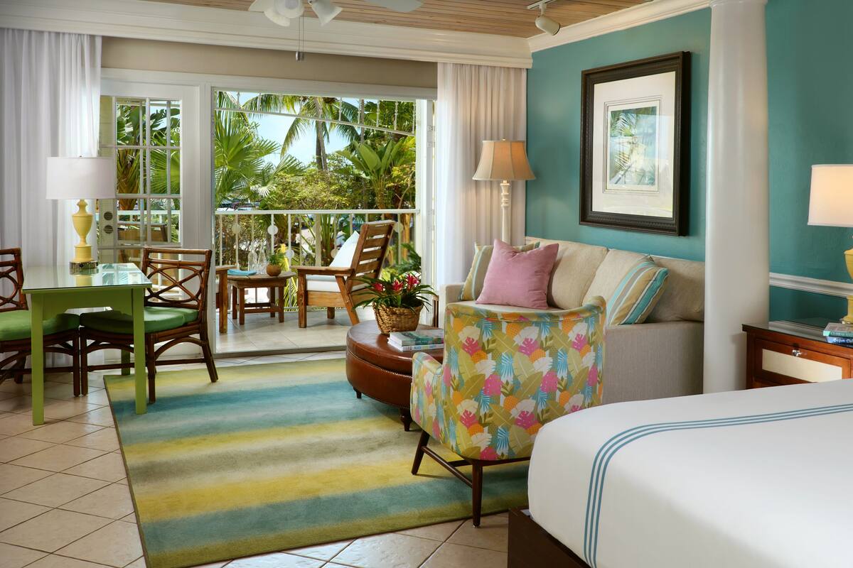 A hotel room with a balcony, a sofa, a bed, and a dining area with chairs and a table.