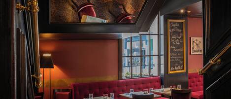 Un interior de restaurante con asientos tapizados en rojo, techo negro y un menú en pizarra.